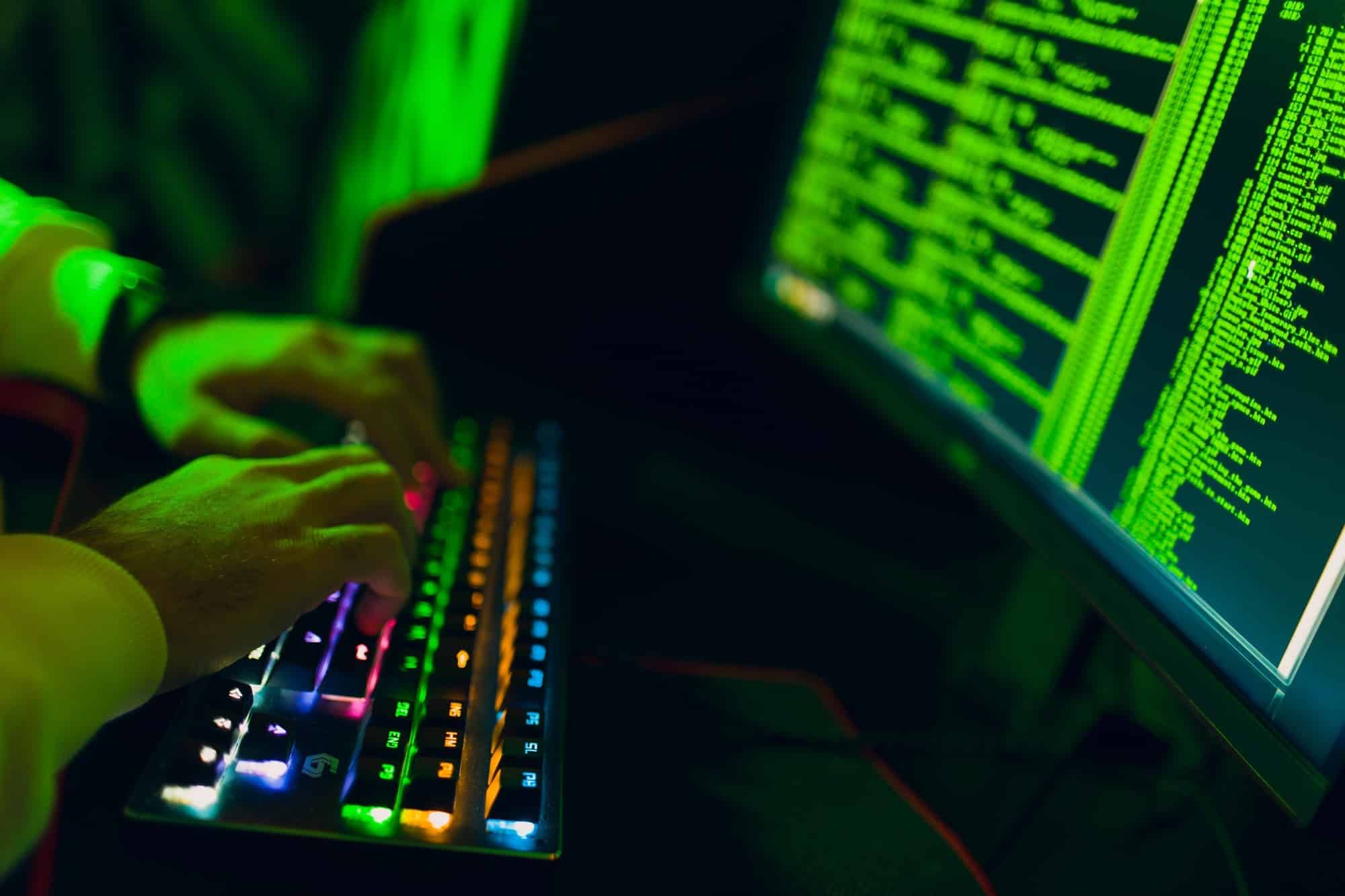 Hacker in hoodie working hacks code site on personal computer with green light