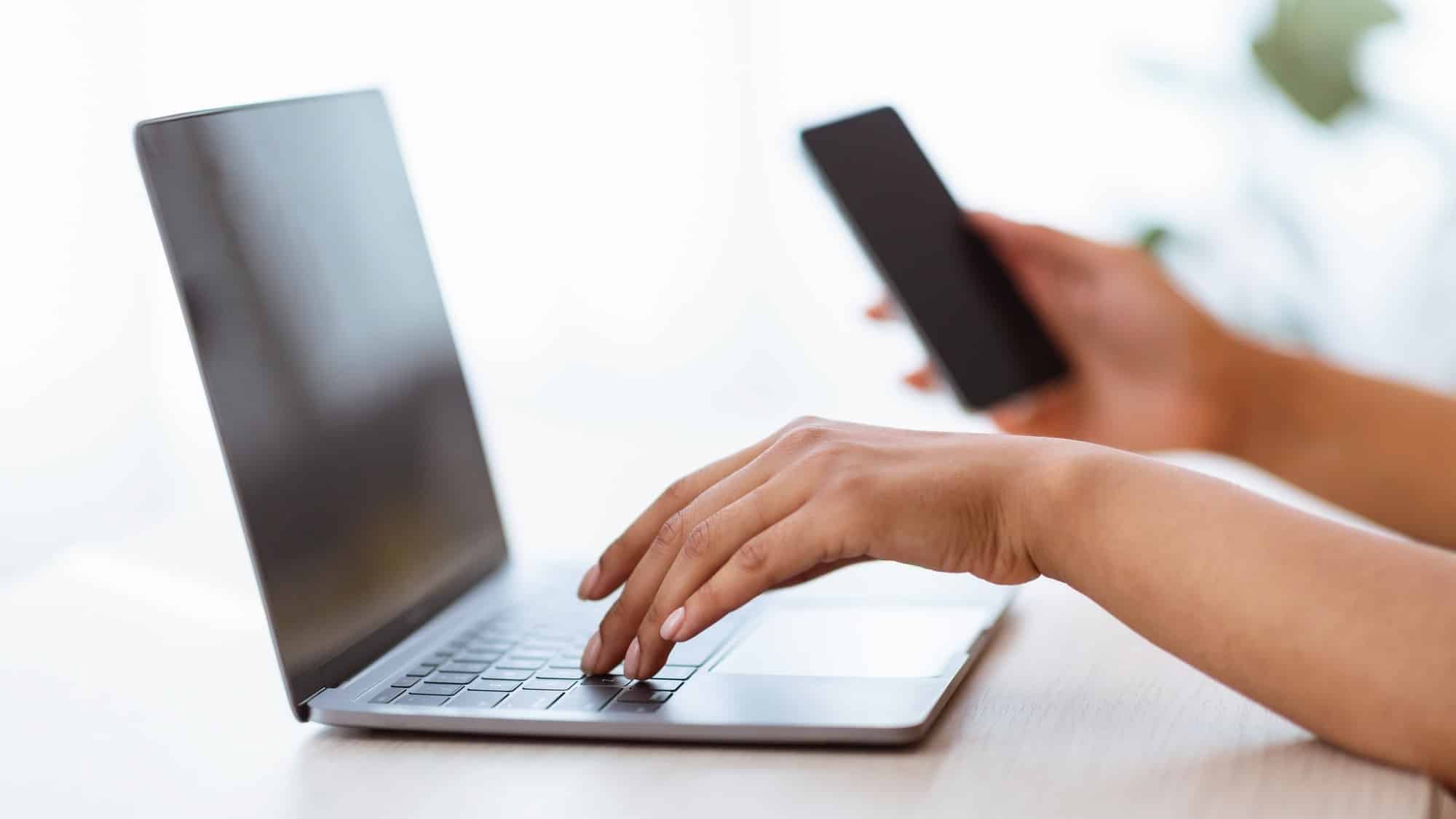 African American Woman Using Smartphone And Typing On Keyboard