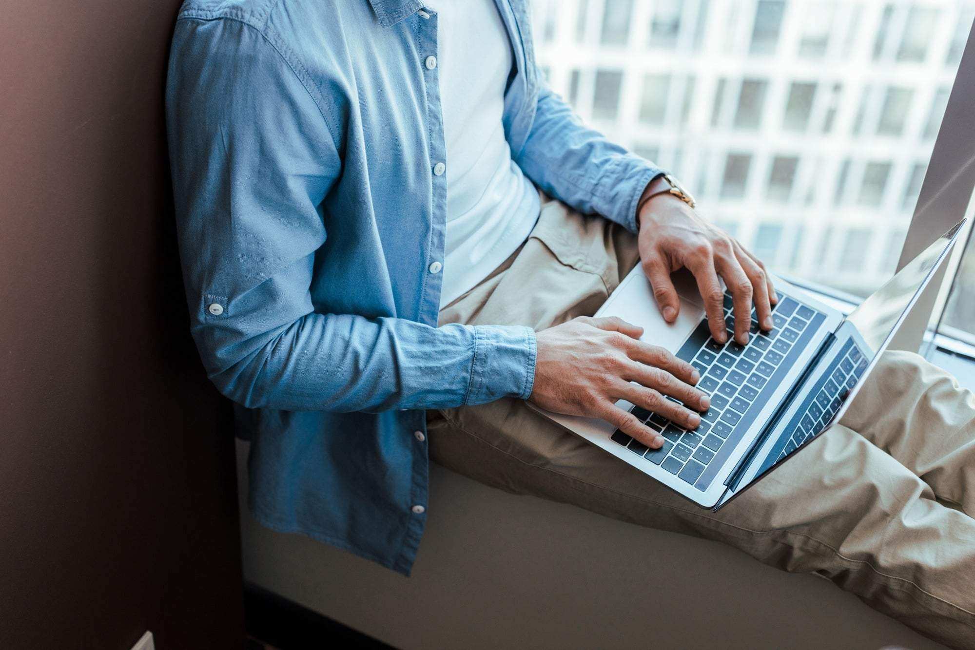 Cropped view of IT worker using laptop on windowsill near window