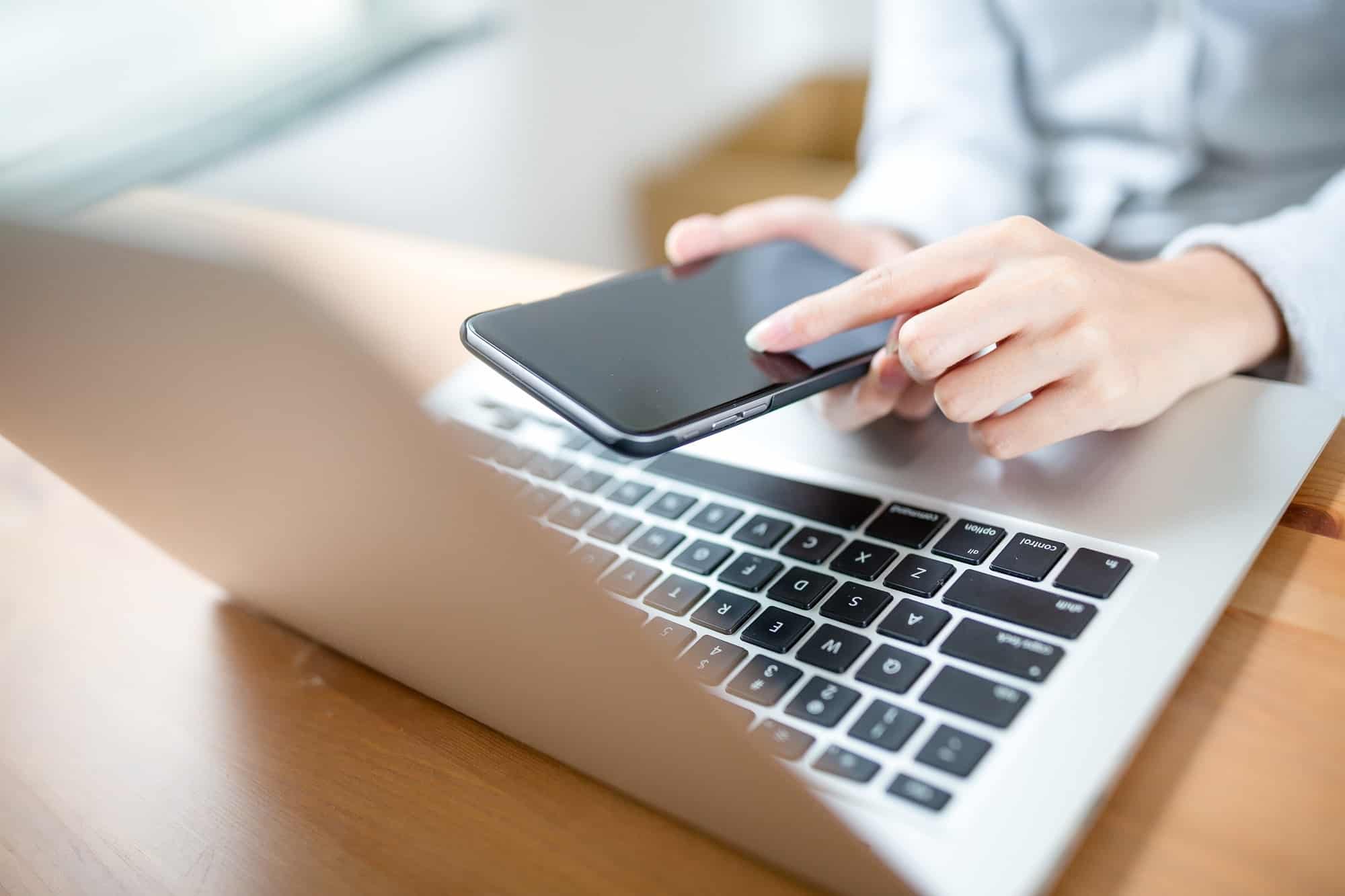 Woman hand touch phone over laptop keyboard