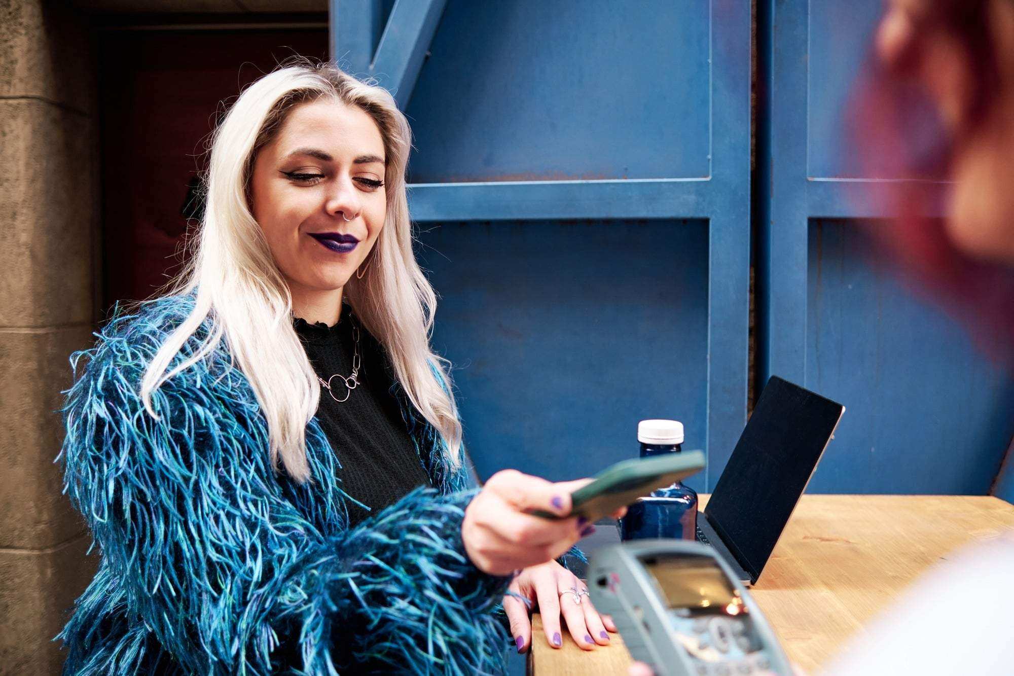 Alternative woman paying the bill through mobile phone using NFC technology.