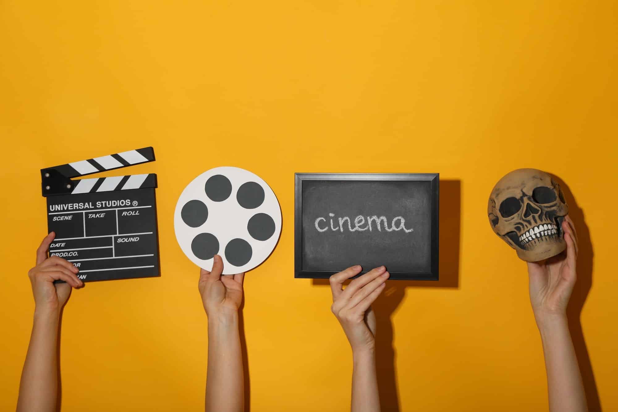 Blackboard with text, reel, skull and clapperboard in hands on yellow background