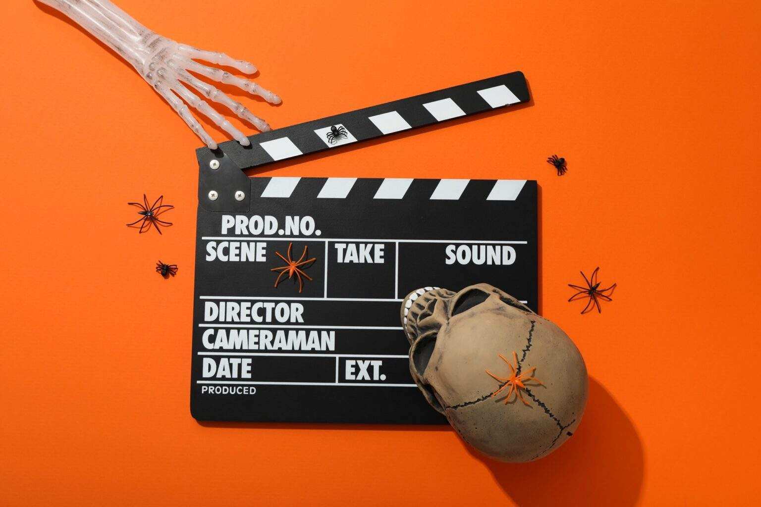 Clapperboard and Halloween decorations on orange background, top view