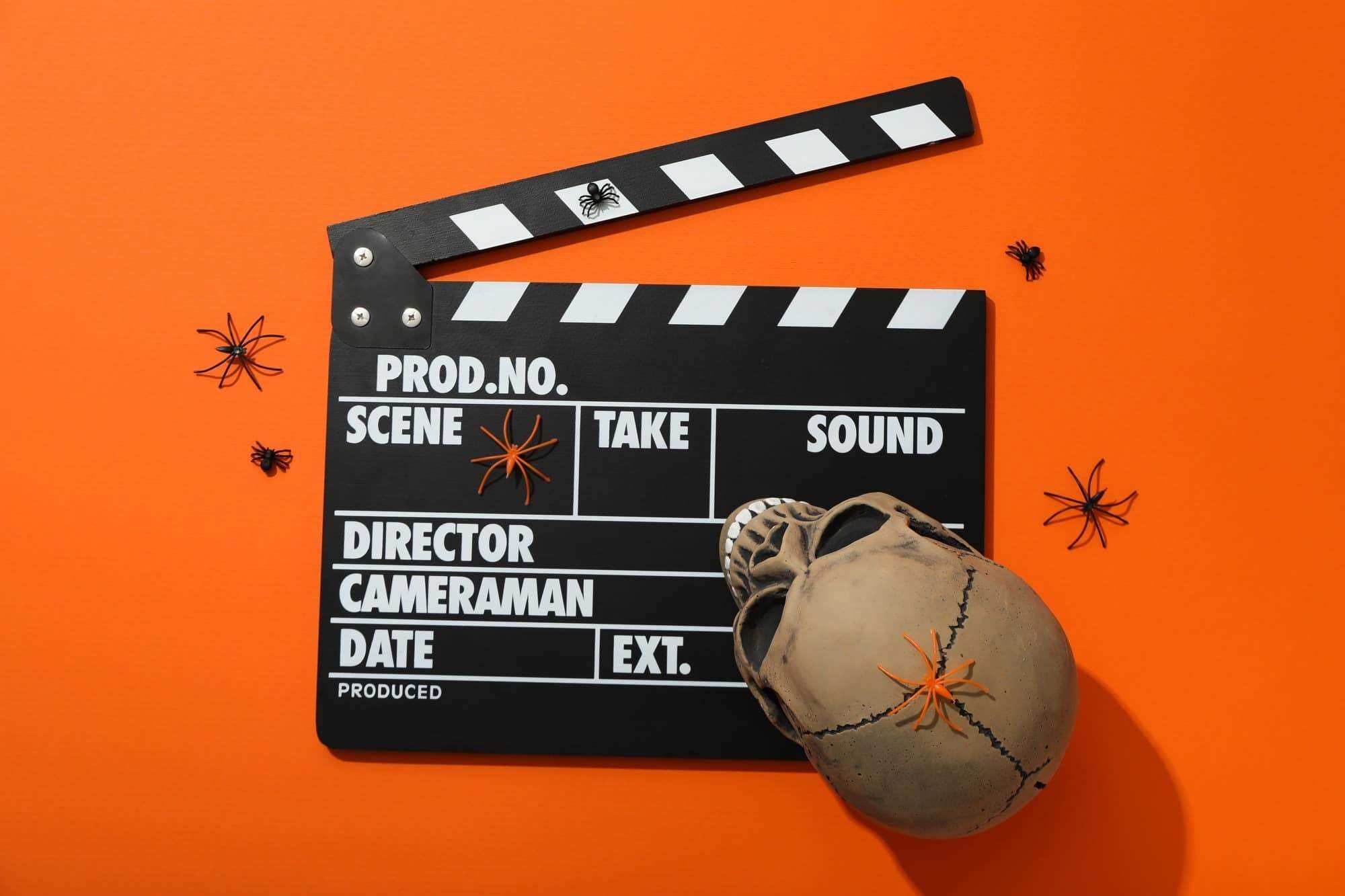 Clapperboard and Halloween decorations on orange background, top view