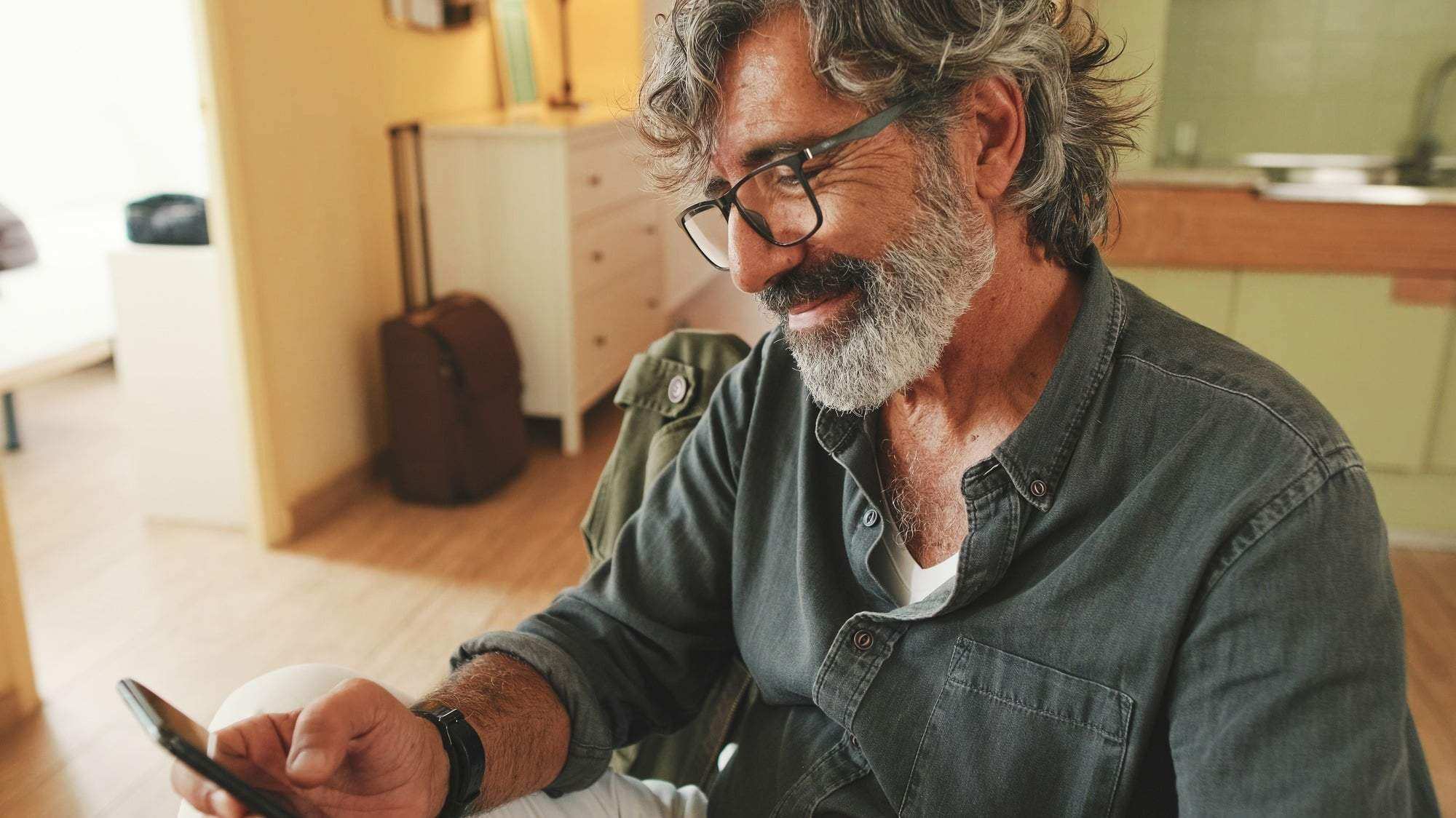 Close-up of an elderly man attentively reading message on his smartphone and drinking coffee