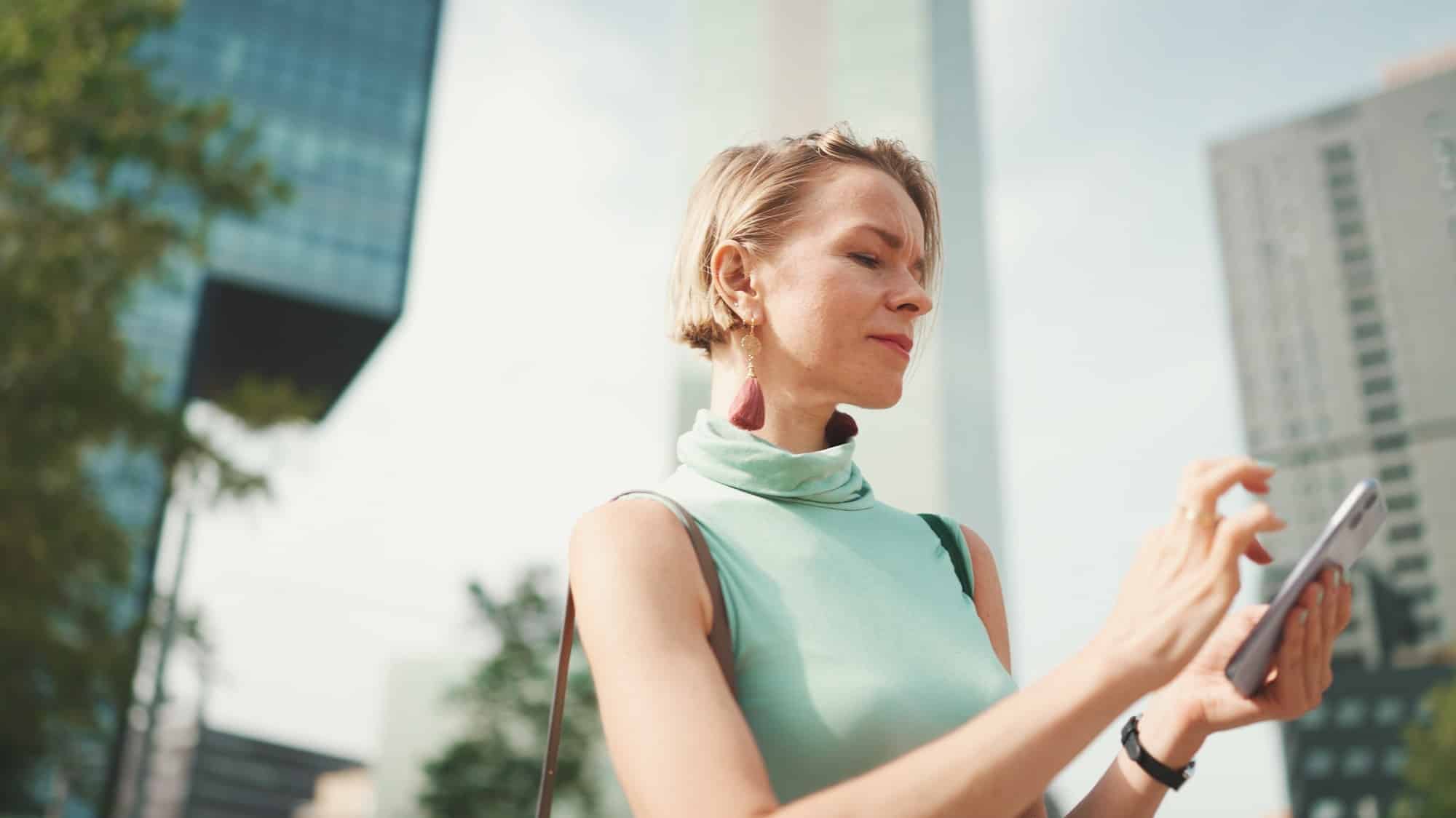 Friendly woman with short blonde hair looking at map trying to find his way using his mobile phone