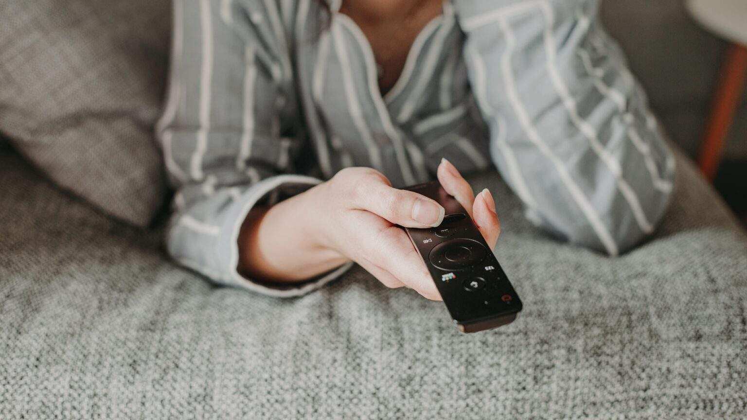 a woman lying on a sofa and watching tv, using the remote control