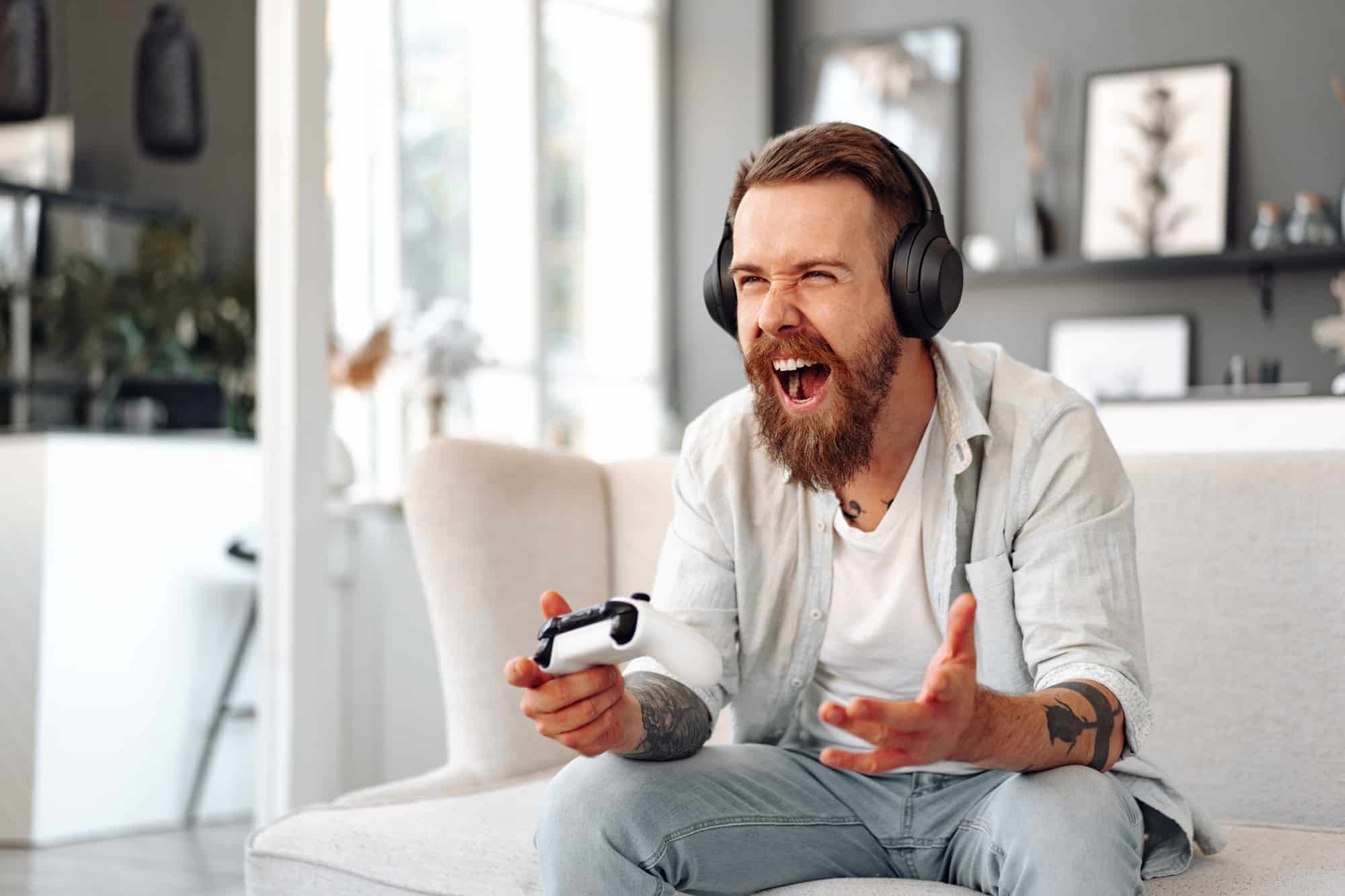 Young bearded man playing video games while sitting on the couch at home