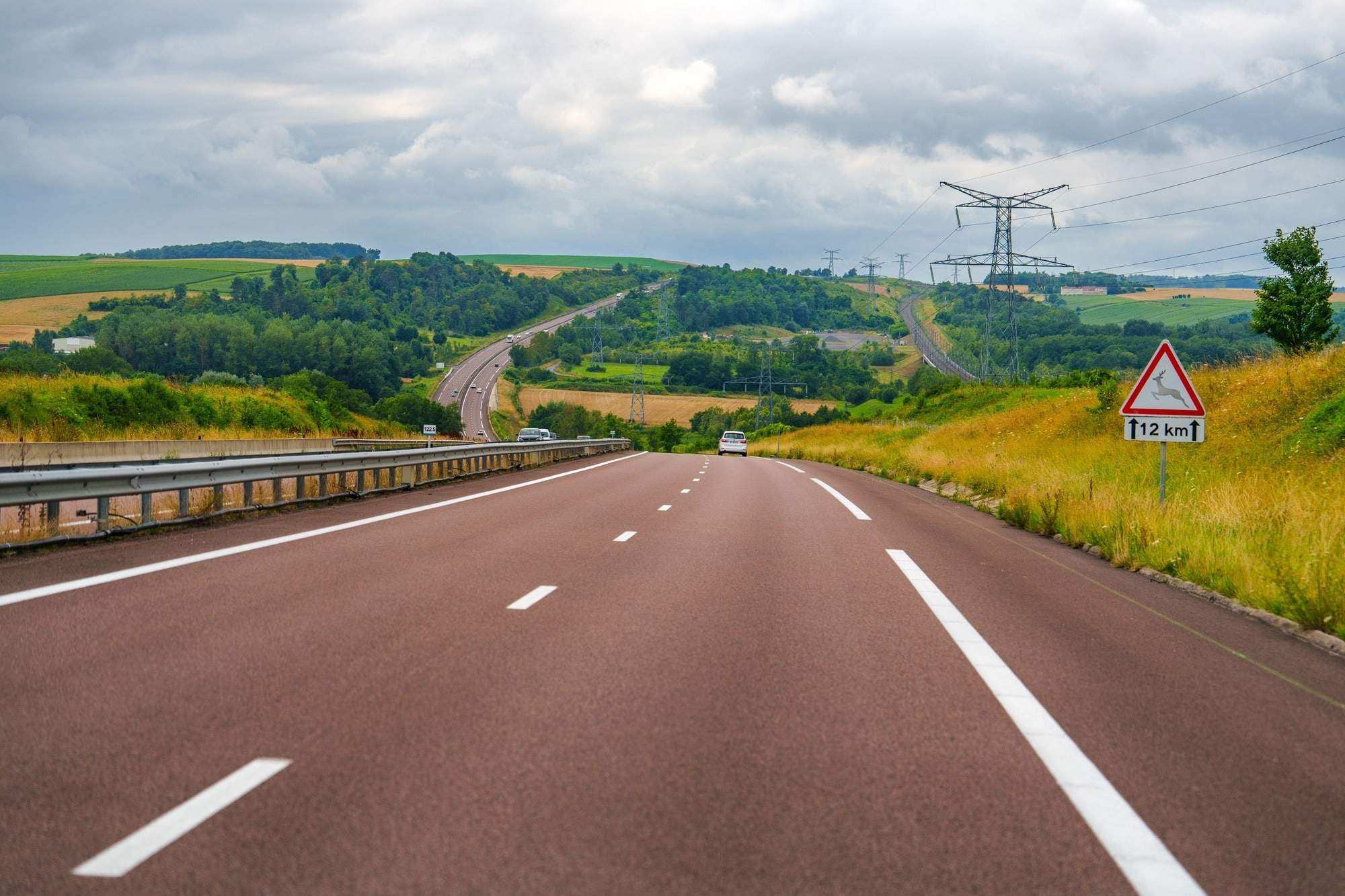 France, Two-lane highway winds through the countryside with green fields and a cloudy sky