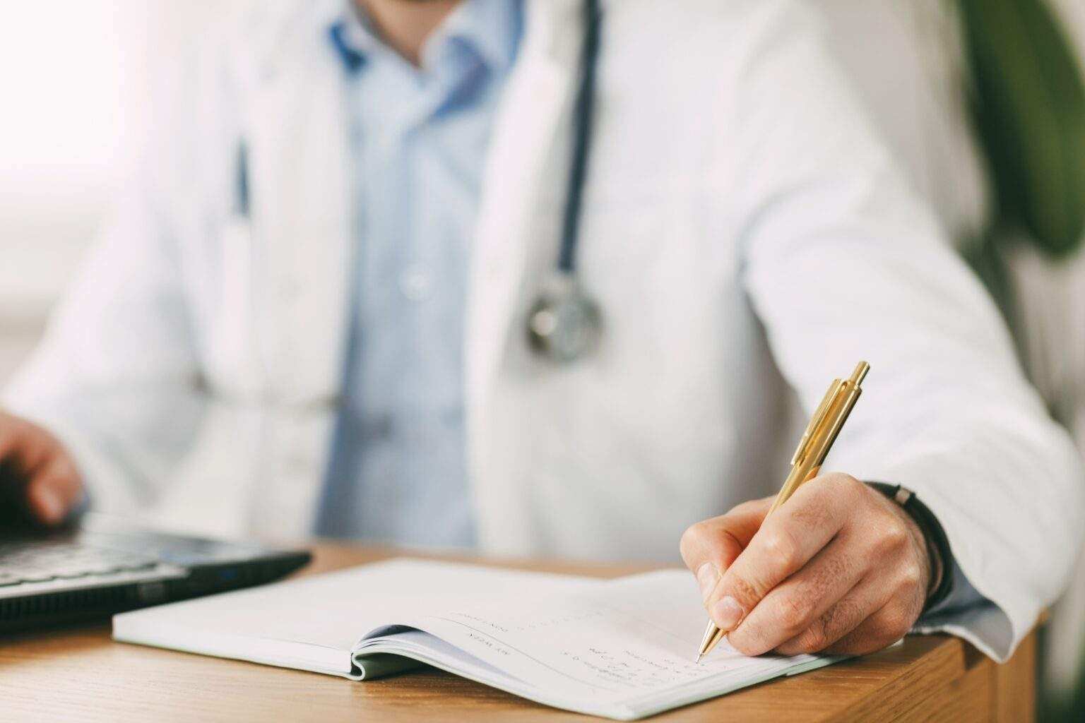 A young doctor of oriental appearance works while sitting at the table in the network with a laptop