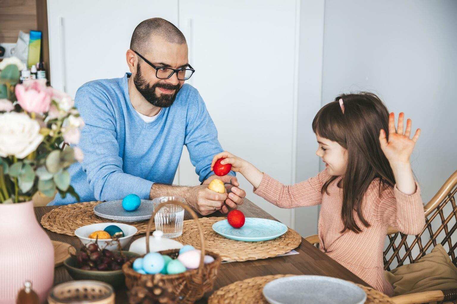 Little girl and her father playing an egg fight game with red Easter eggs