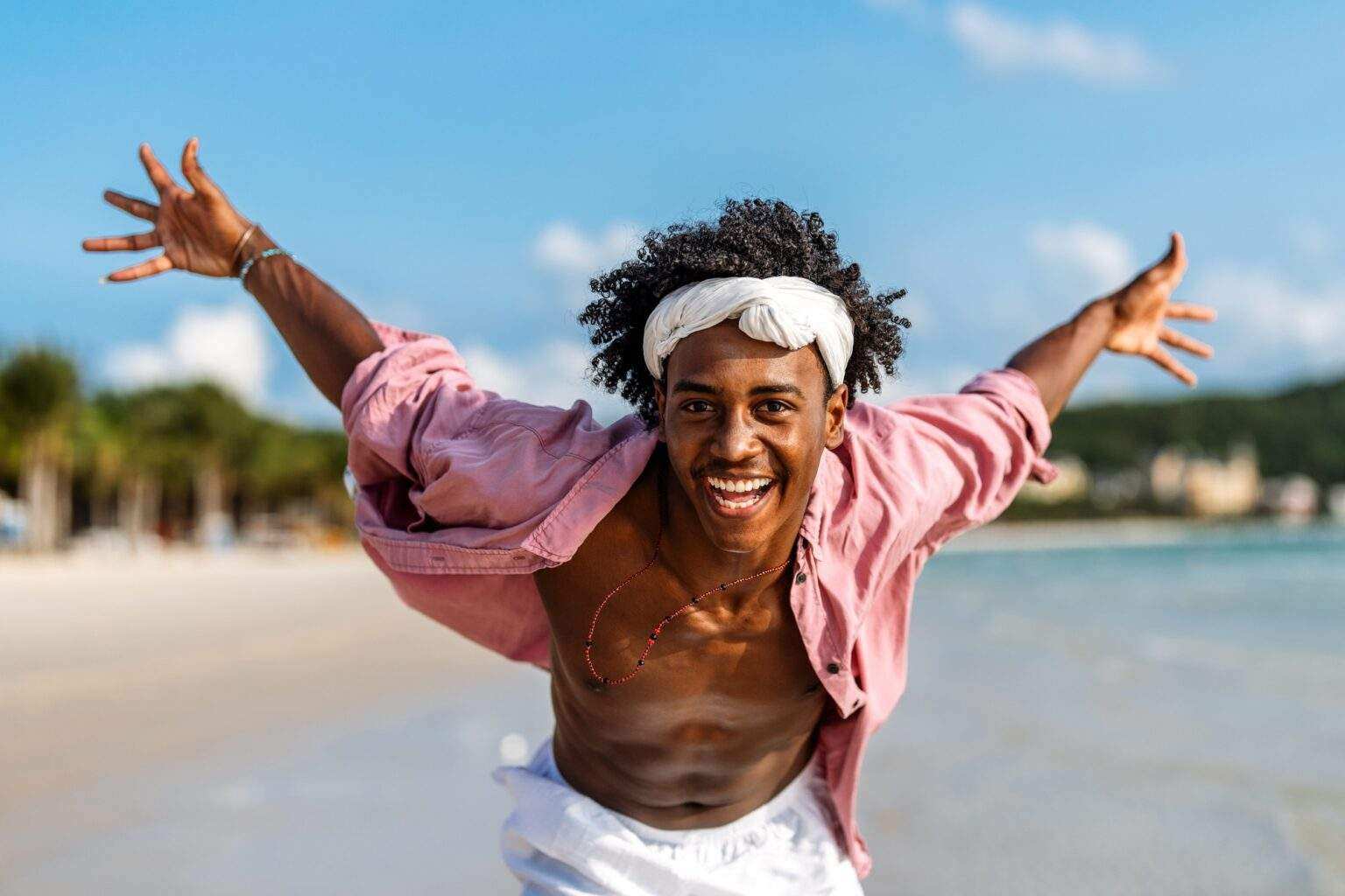 Young Black man enjoying a sunny beach day, running through ocean waves, smiling and feeling free